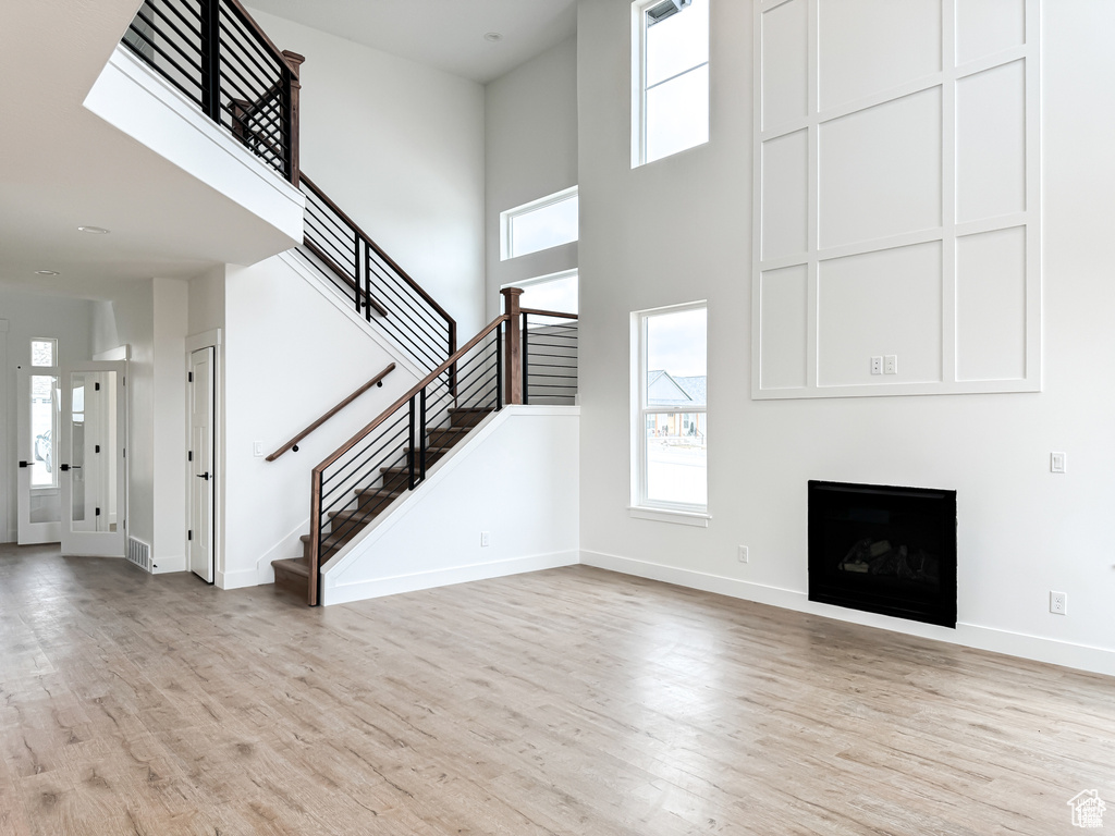 Unfurnished living room featuring light wood finished floors, healthy amount of natural light, and a towering ceiling