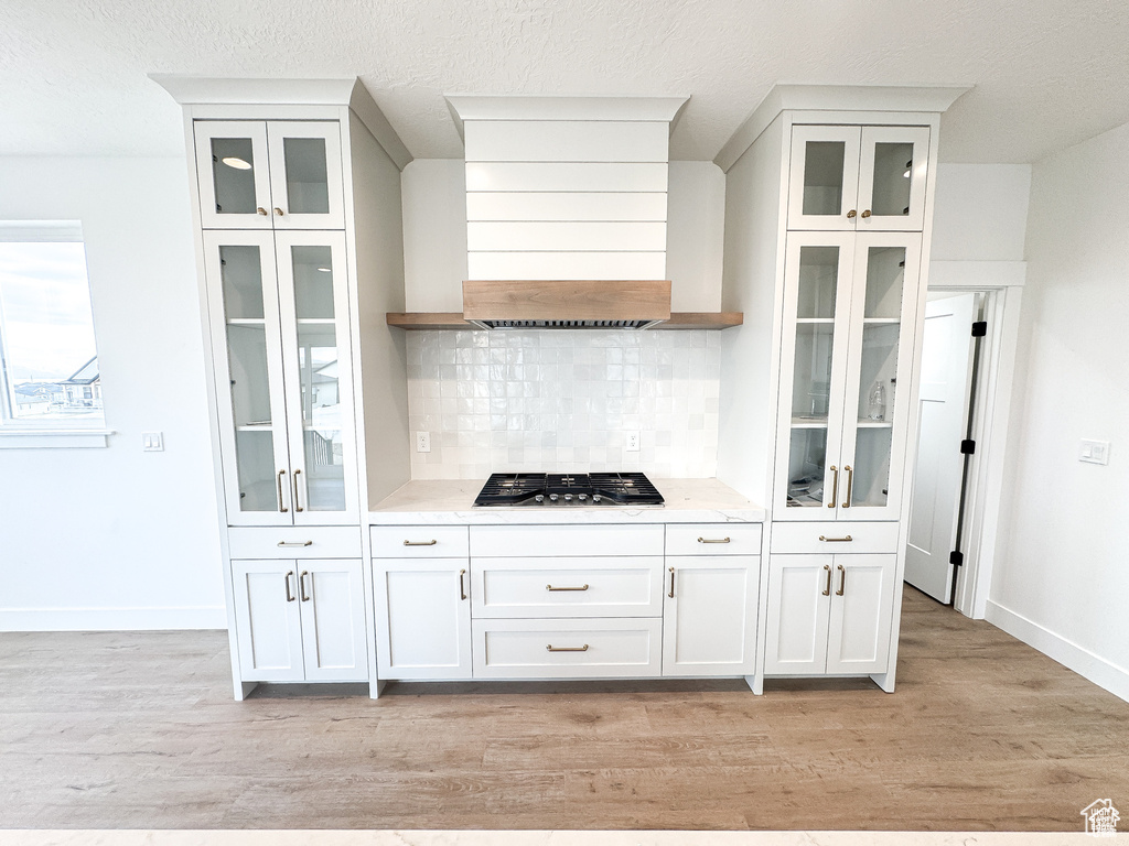 Kitchen with stainless steel gas cooktop, backsplash, light wood-style flooring, baseboards, and premium range hood