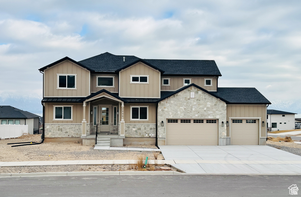 View of front facade with a standing seam roof, stone siding, an attached garage, and a shingled roof