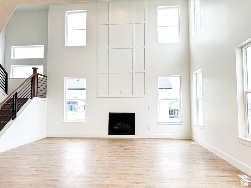 Unfurnished living room with a high ceiling, wood finished floors, baseboards, and healthy amount of natural light