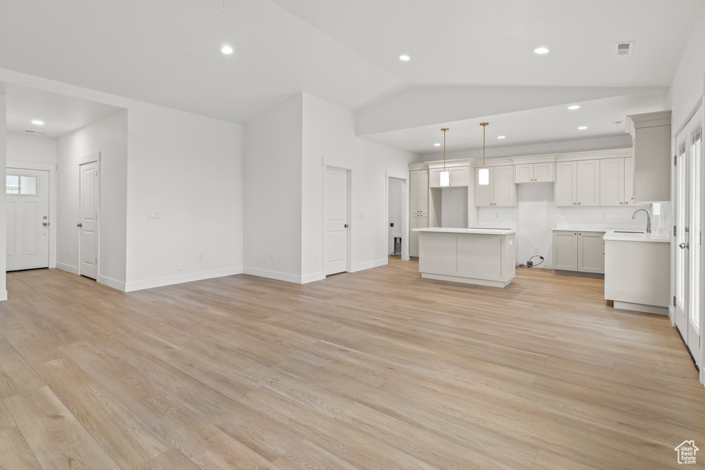 Unfurnished living room with vaulted ceiling, light wood-style floors, recessed lighting, a sink, and baseboards