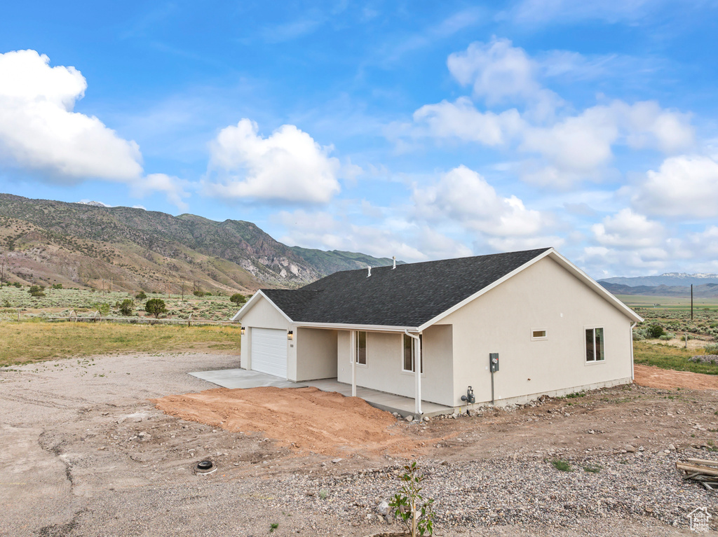 View of property exterior featuring a mountain view, a garage, stucco siding, a shingled roof, and driveway