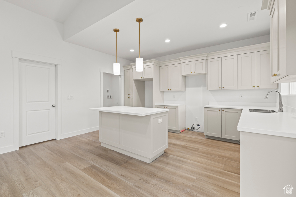 Kitchen with a sink, a kitchen island, light wood-style floors, recessed lighting, and decorative light fixtures