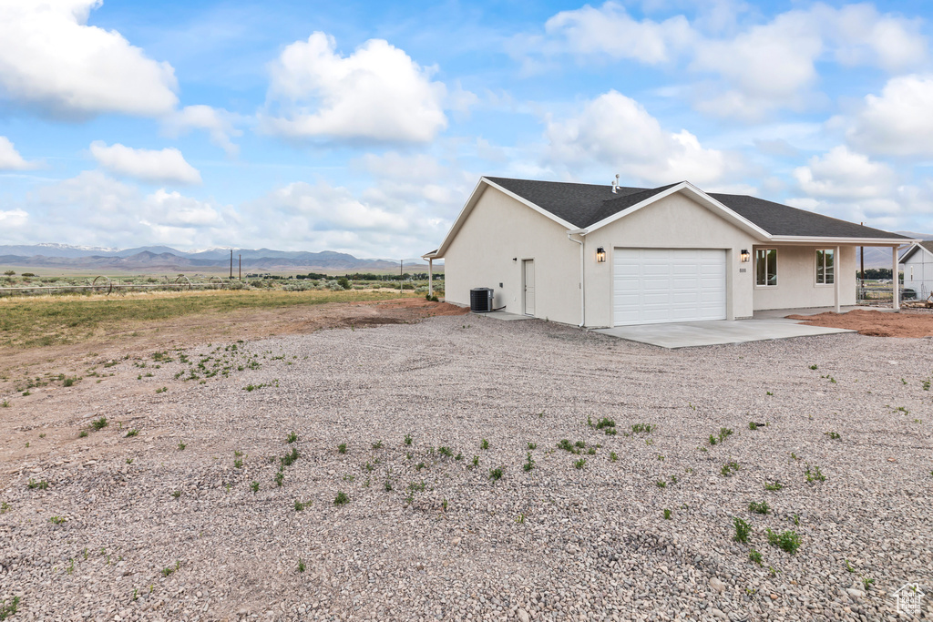 View of side of home featuring driveway, an attached garage, a mountain view, cooling unit, and stucco siding