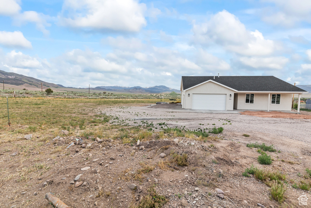 View of side of home with a garage, a mountain view, dirt driveway, and a rural view