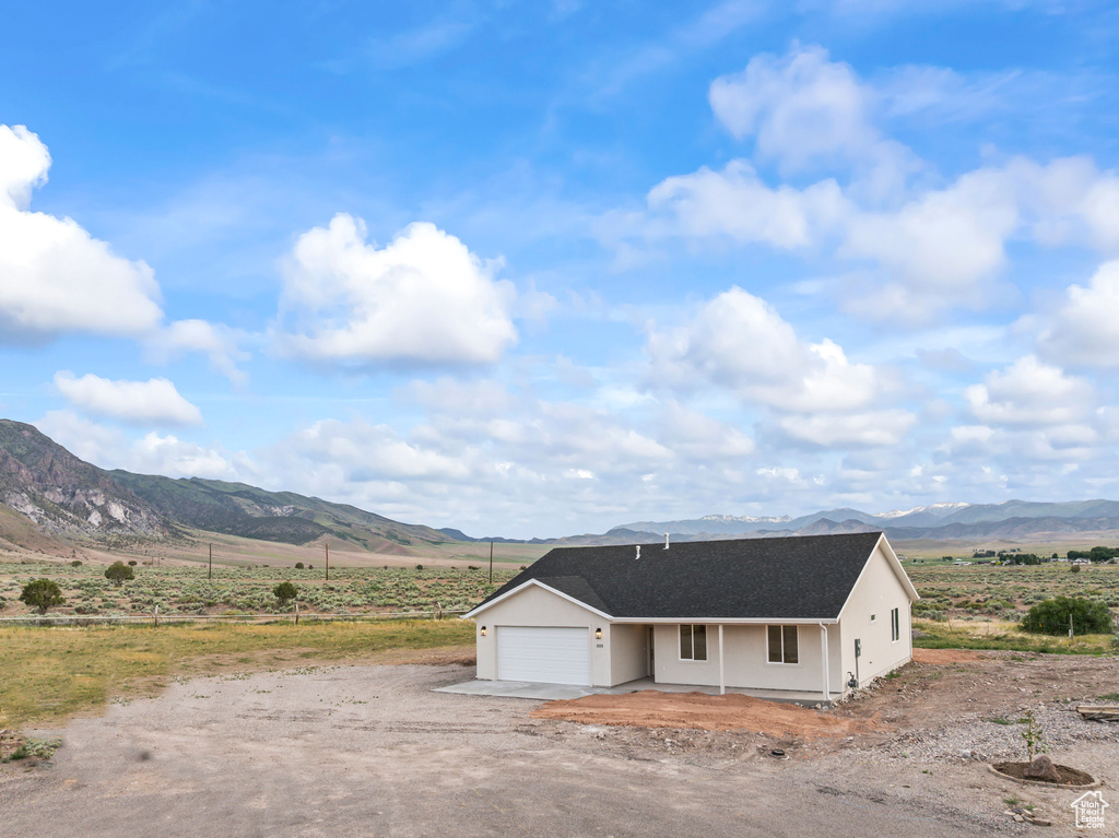 View of front of home with a mountain view, a view of countryside, an attached garage, and roof with shingles