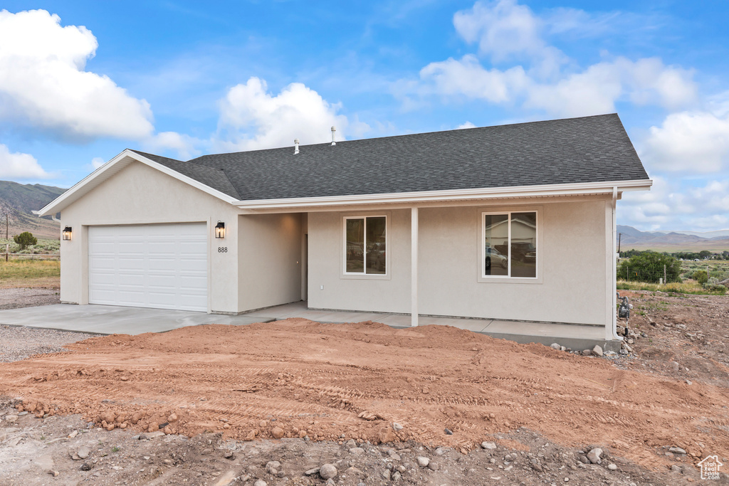 Ranch-style house featuring a mountain view, dirt driveway, an attached garage, and roof with shingles
