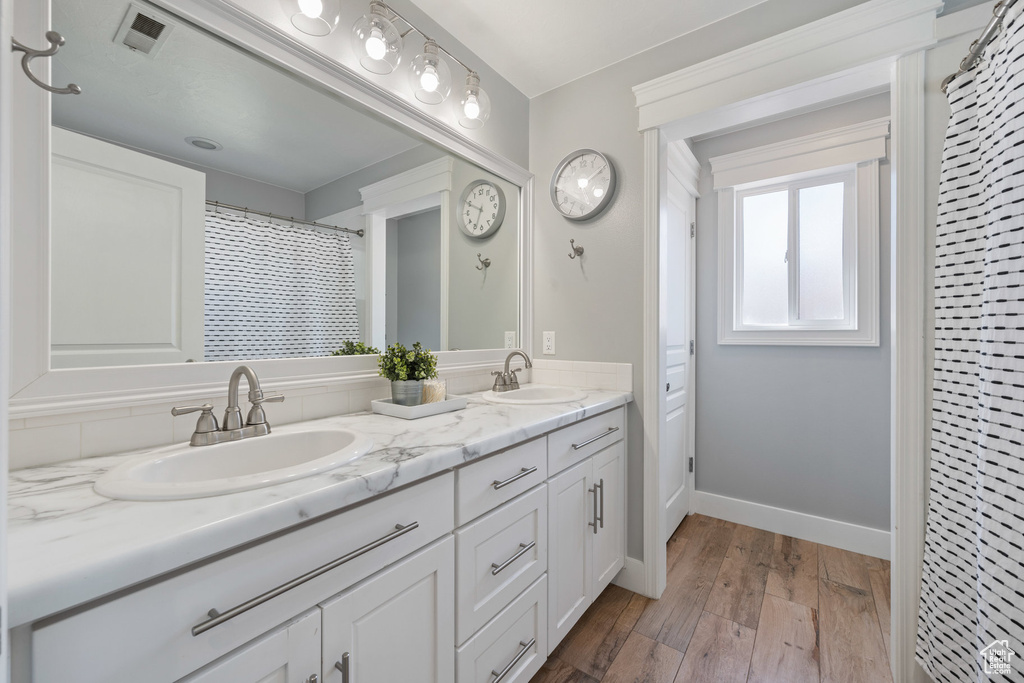 Full bathroom featuring double vanity, wood finished floors, and baseboards