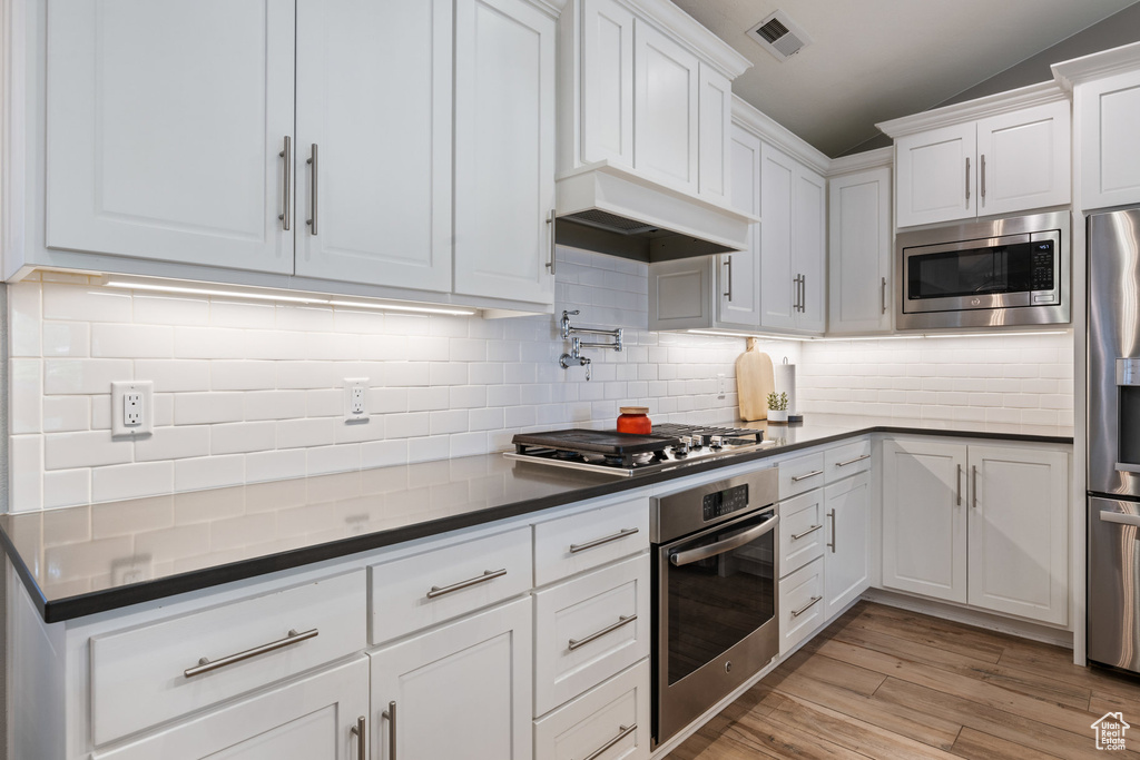 Kitchen with stainless steel appliances, white cabinetry, dark countertops, and decorative backsplash