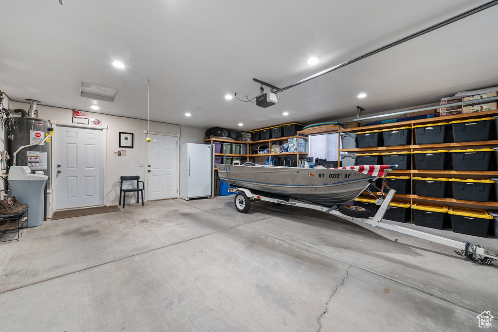 Garage with freestanding refrigerator, a garage door opener, gas water heater, and recessed lighting