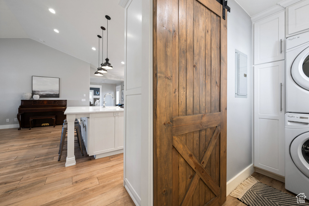 Laundry area featuring estacked washer and dryer, a barn door, cabinet space, light wood-style flooring, and recessed lighting