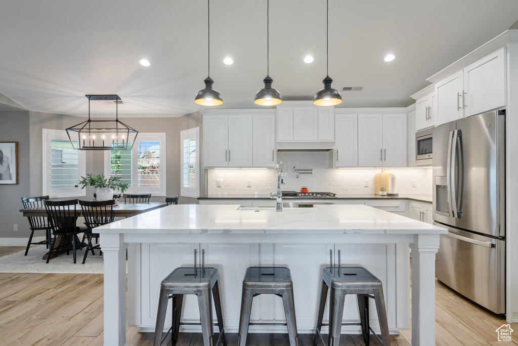 Kitchen featuring appliances with stainless steel finishes, a sink, light wood-style floors, tasteful backsplash, and white cabinetry