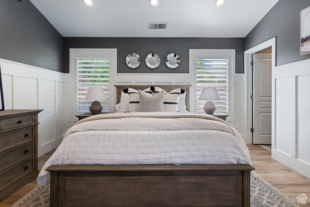 Bedroom with wainscoting, a decorative wall, multiple windows, wood finished floors, and recessed lighting