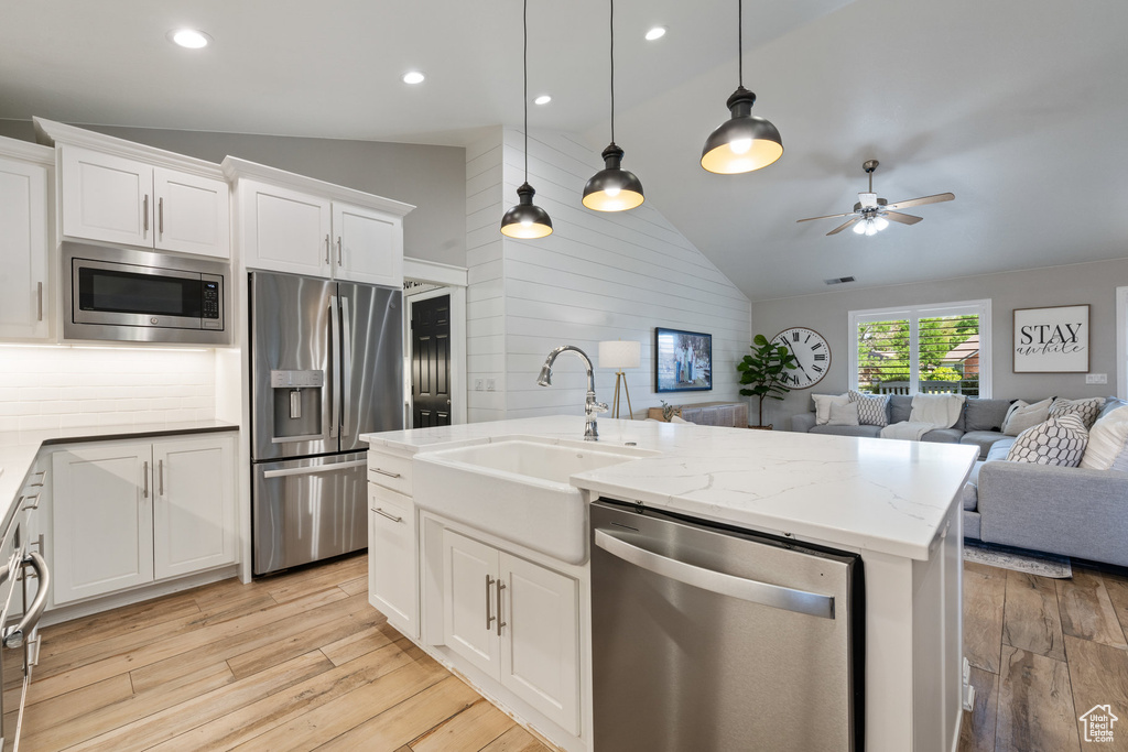 Kitchen featuring stainless steel appliances, vaulted ceiling, open floor plan, a sink, and light wood finished floors