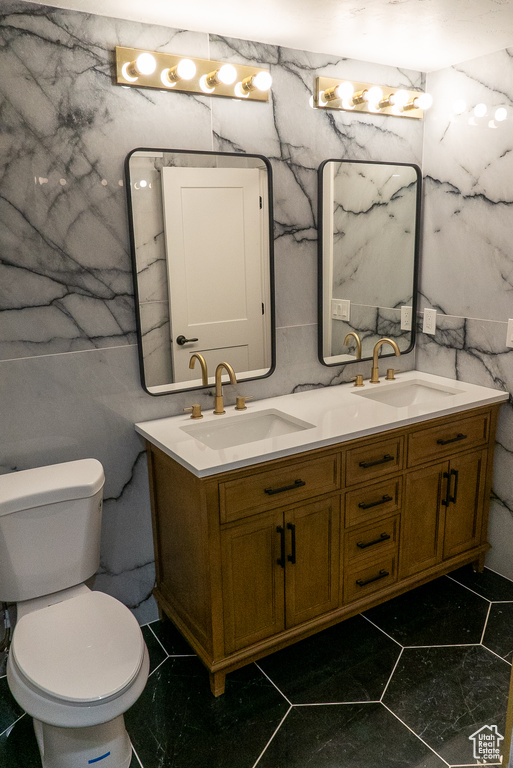 Bathroom featuring double vanity, toilet, tile walls, and tile patterned flooring