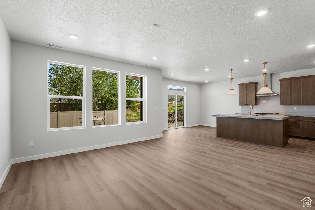 Kitchen with wall chimney exhaust hood, light wood-style flooring, a center island with sink, tasteful backsplash, and recessed lighting