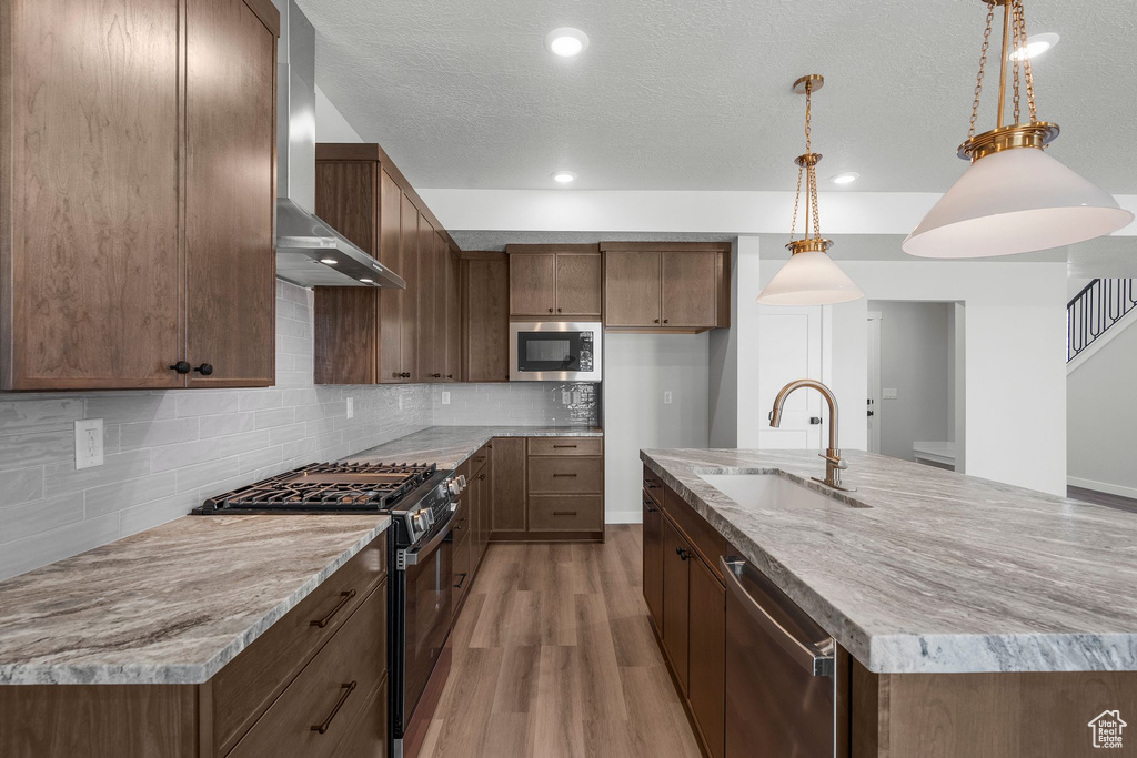 Kitchen featuring stainless steel appliances, a sink, wall chimney range hood, light wood-style floors, and backsplash