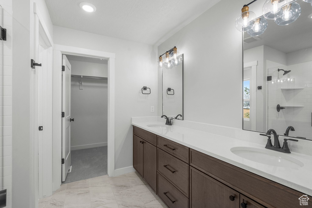 Full bathroom with double vanity, a spacious closet, a stall shower, marble finish floors, and baseboards