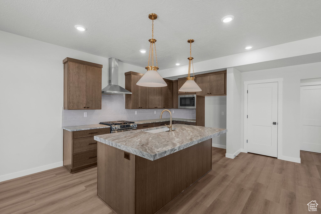Kitchen featuring wall chimney exhaust hood, a sink, baseboards, appliances with stainless steel finishes, and light wood-style floors