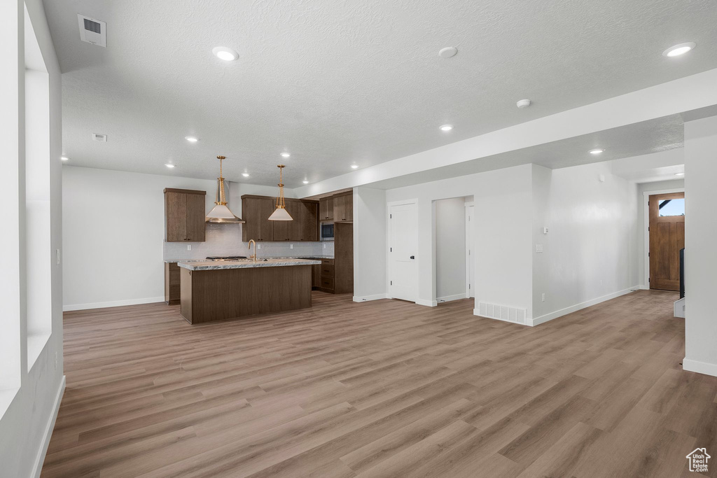 Kitchen with open floor plan, wall chimney exhaust hood, baseboards, stainless steel microwave, and light wood finished floors