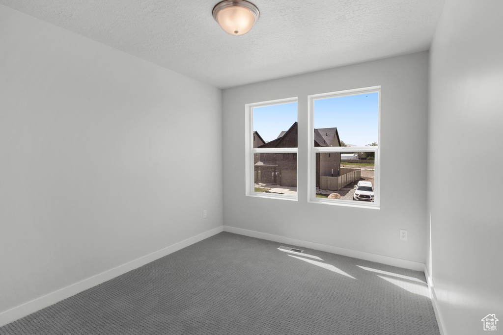 Spare room featuring carpet flooring, baseboards, and a textured ceiling