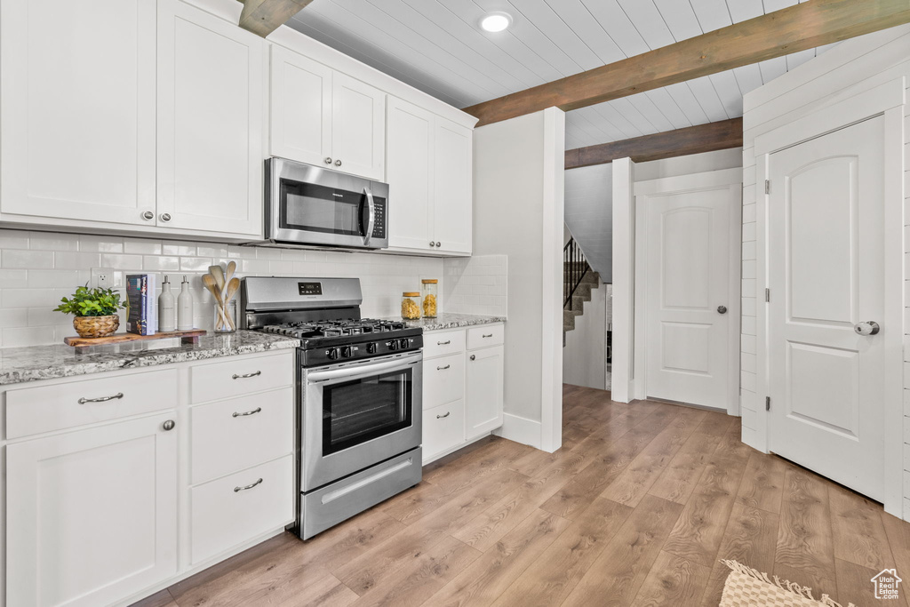 Kitchen with stainless steel appliances, tasteful backsplash, light wood finished floors, white cabinetry, and wood ceiling