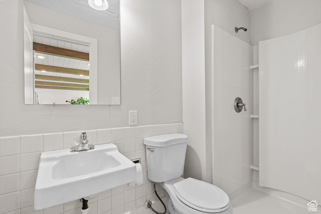 Full bath with a shower stall, toilet, a sink, tile walls, and wainscoting