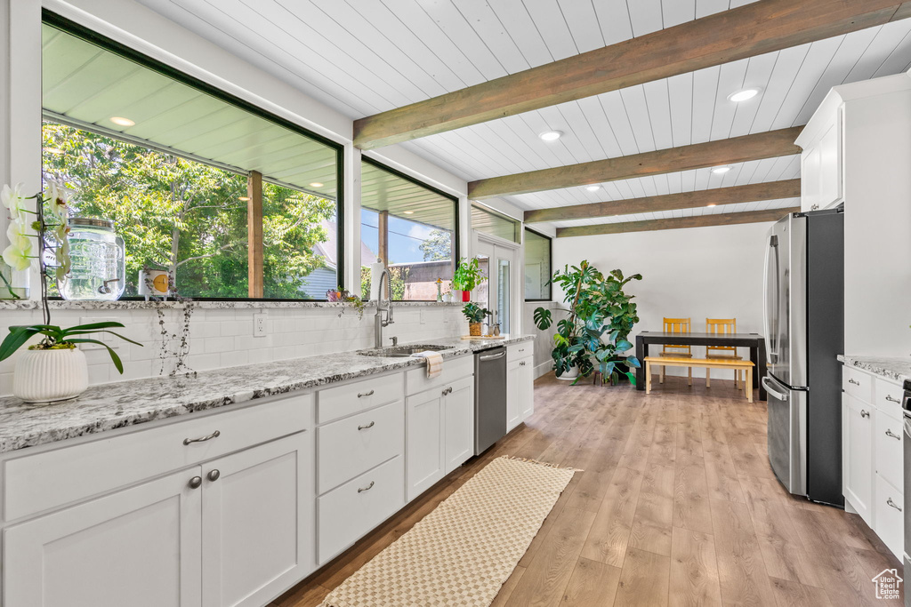 Kitchen with appliances with stainless steel finishes, a sink, white cabinets, beam ceiling, and light wood-style flooring