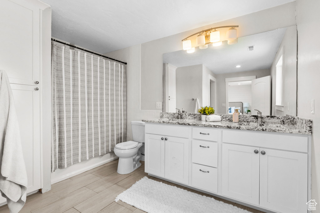 Full bathroom with double vanity, toilet, a shower with shower curtain, and wood finished floors