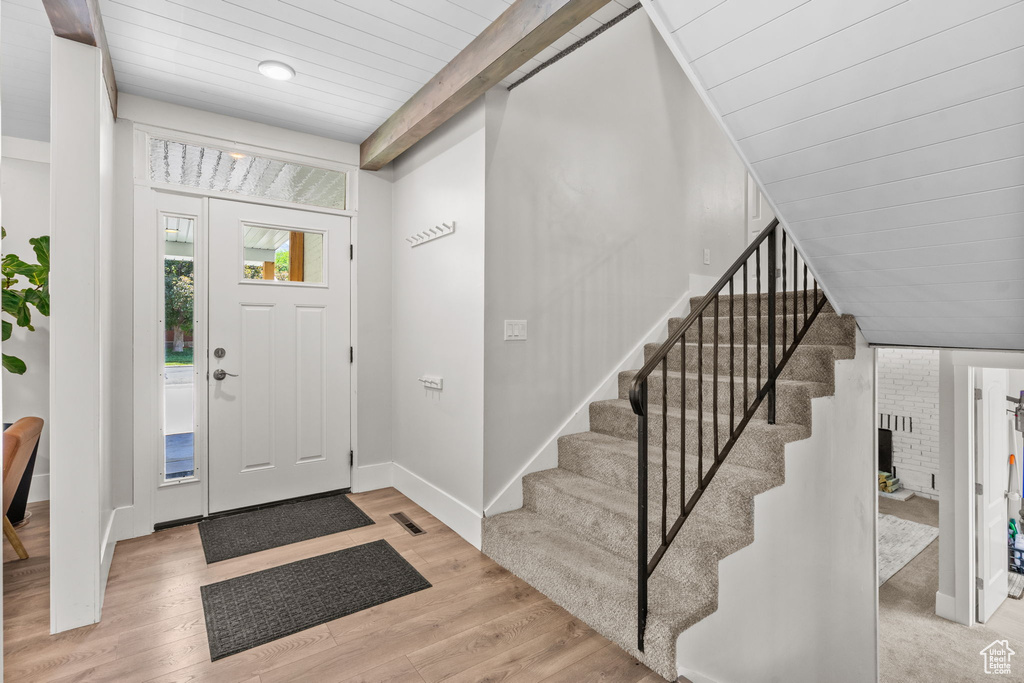 Foyer featuring stairway, light wood-style flooring, wooden ceiling with exposed beams, and baseboards