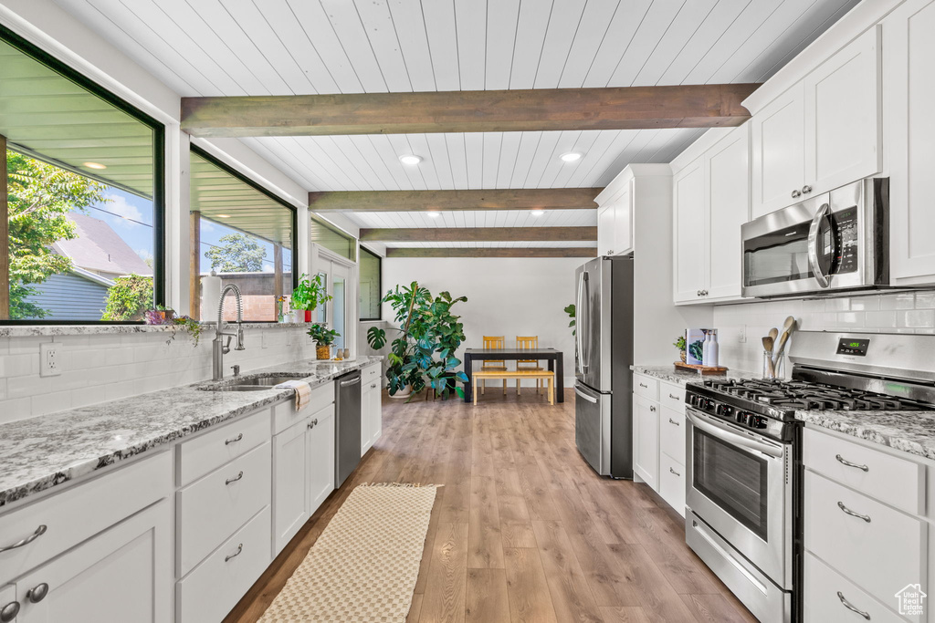 Kitchen featuring stainless steel appliances, a sink, white cabinets, wooden ceiling with exposed beams, and light wood finished floors