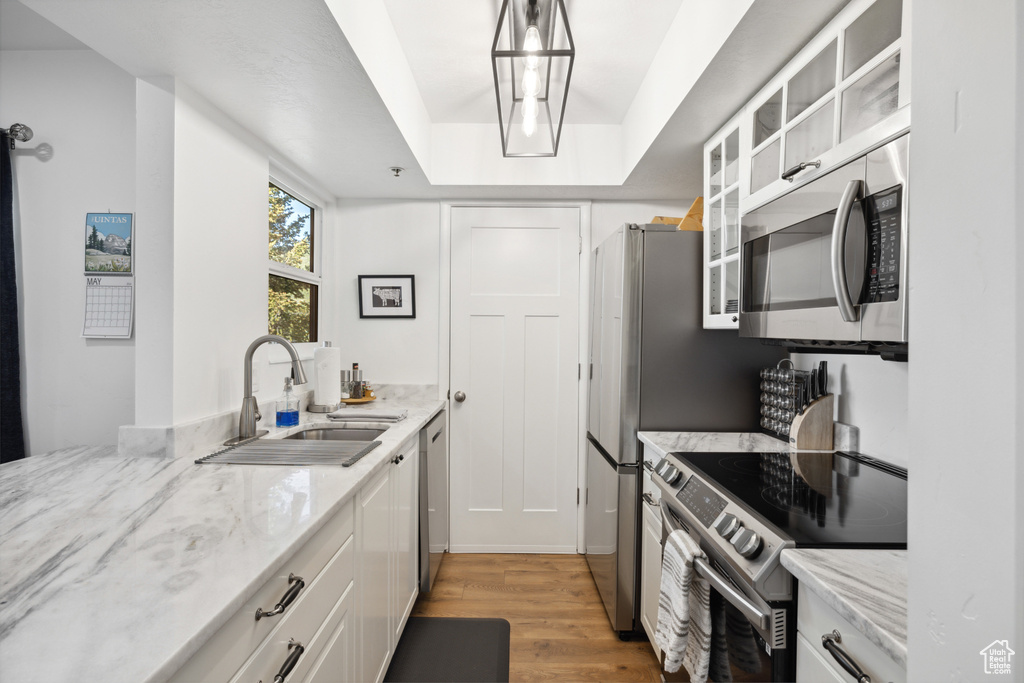 Kitchen featuring stainless steel appliances, a sink, light wood-style floors, white cabinetry, and glass insert cabinets