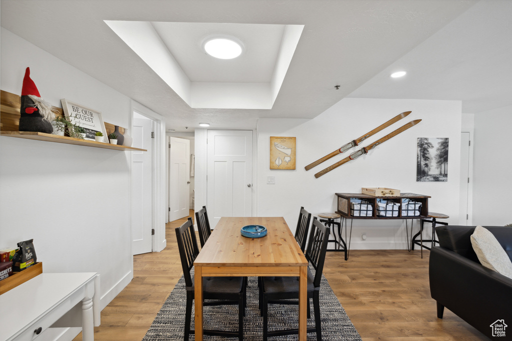 Dining area with light wood finished floors, baseboards, a tray ceiling, and recessed lighting