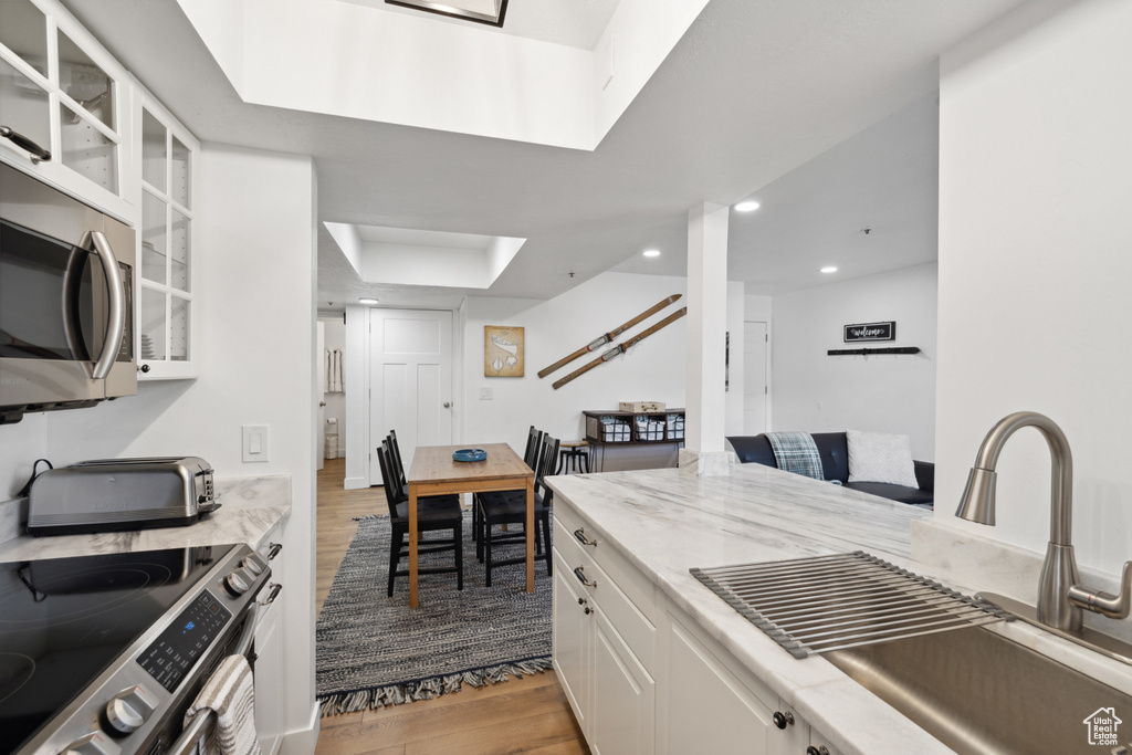Kitchen with a sink, stainless steel appliances, light wood finished floors, white cabinets, and glass insert cabinets