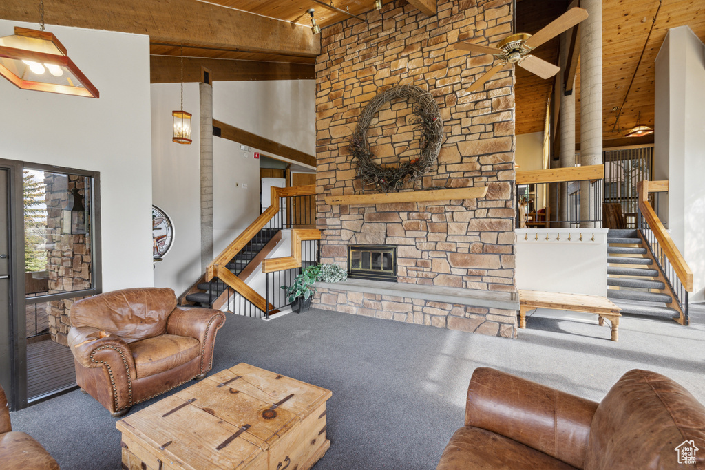 Carpeted living room with wooden ceiling with exposed beams, ceiling fan, a high ceiling, stairway, and a stone fireplace