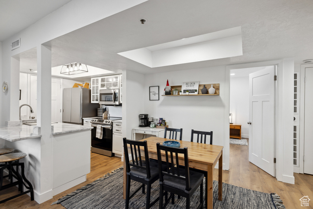 Dining room featuring light wood-style flooring, a raised ceiling, and baseboards