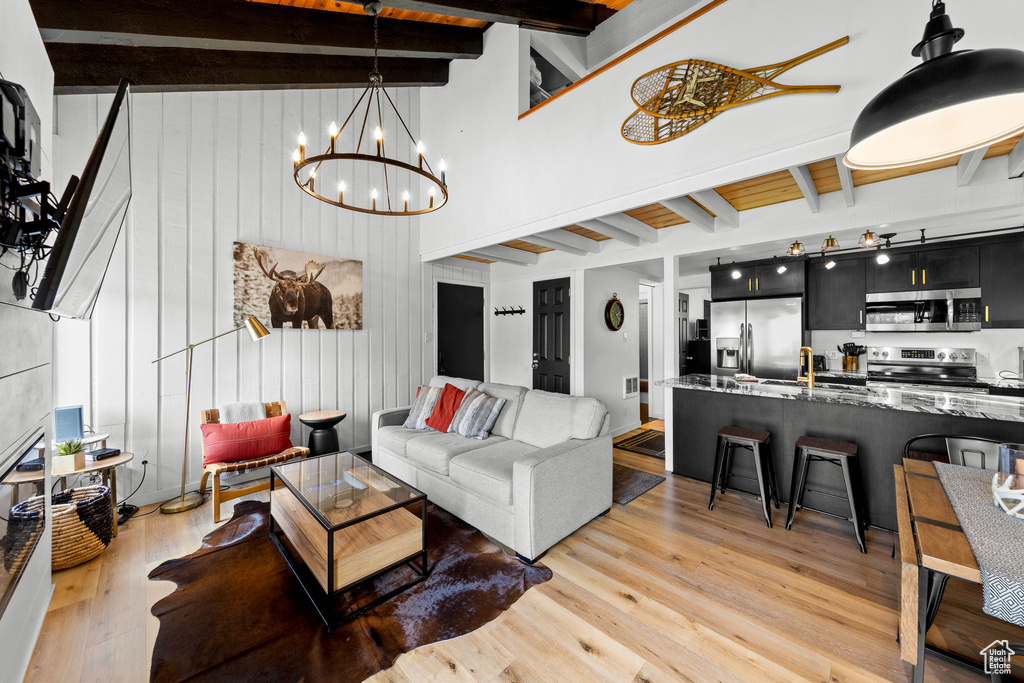 Living area featuring beam ceiling, light wood-style flooring, a chandelier, wooden walls, and a high ceiling