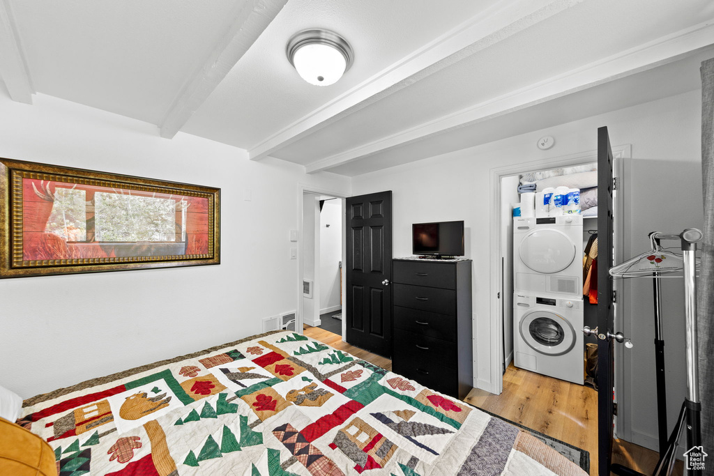 Bedroom with stacked washer and clothes dryer, beam ceiling, and light wood finished floors