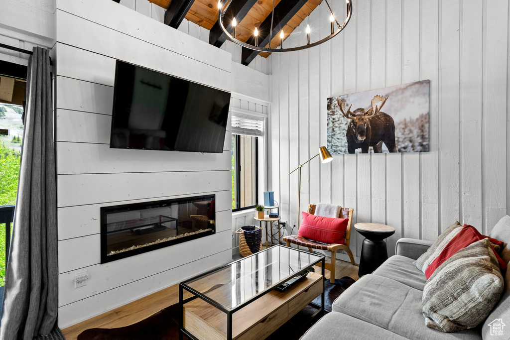 Living area with a glass covered fireplace, beamed ceiling, wood finished floors, wood walls, and a chandelier