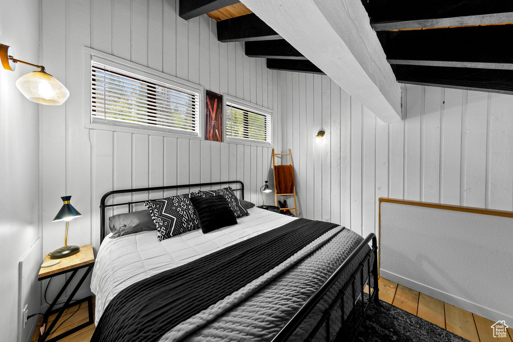 Bedroom featuring wood finished floors, wood walls, and beamed ceiling