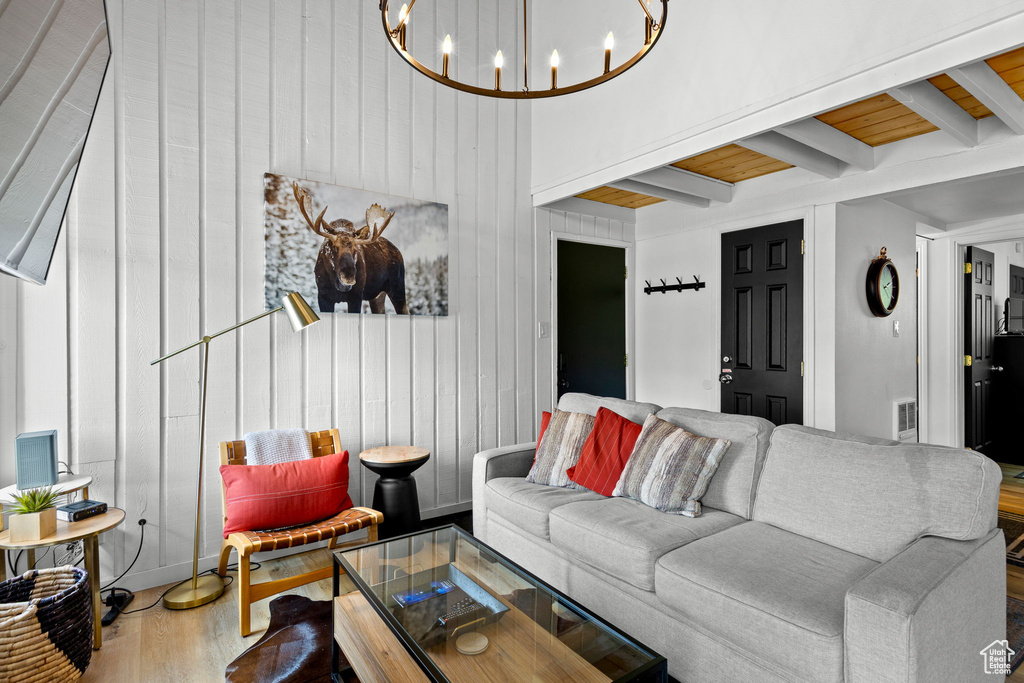 Living room with a chandelier, wood finished floors, beamed ceiling, and wood walls