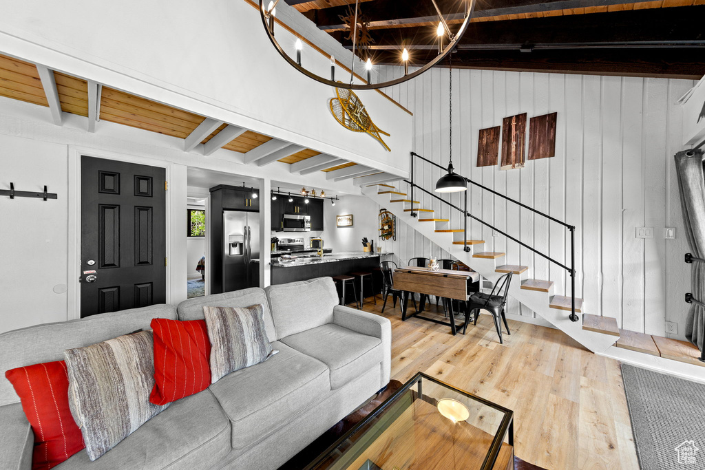 Living room featuring stairway, light wood-style floors, wooden ceiling with exposed beams, and a chandelier