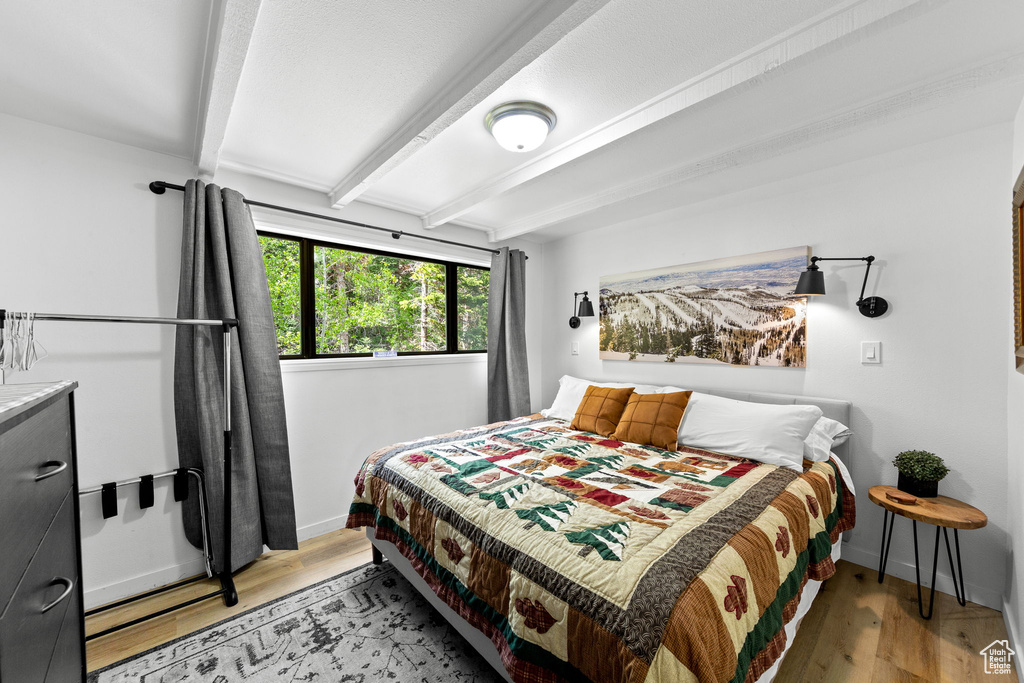 Bedroom featuring beam ceiling, baseboards, and light wood finished floors