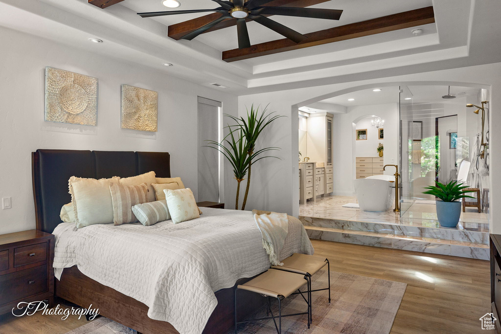 Bedroom featuring a raised ceiling, arched walkways, wood finished floors, recessed lighting, and ensuite bathroom