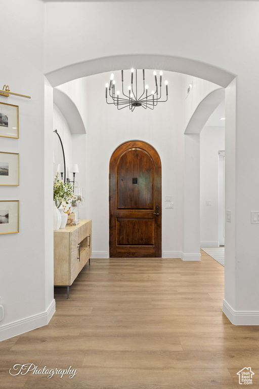 Foyer featuring a chandelier, light wood-style floors, arched walkways, and baseboards