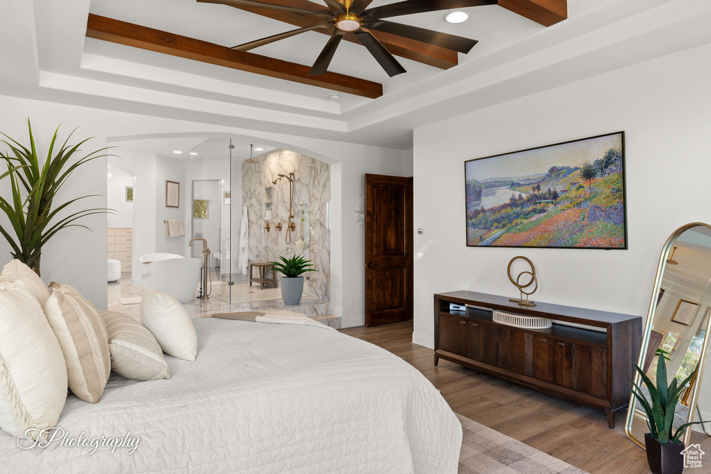 Bedroom with a raised ceiling, arched walkways, connected bathroom, recessed lighting, and wood finished floors