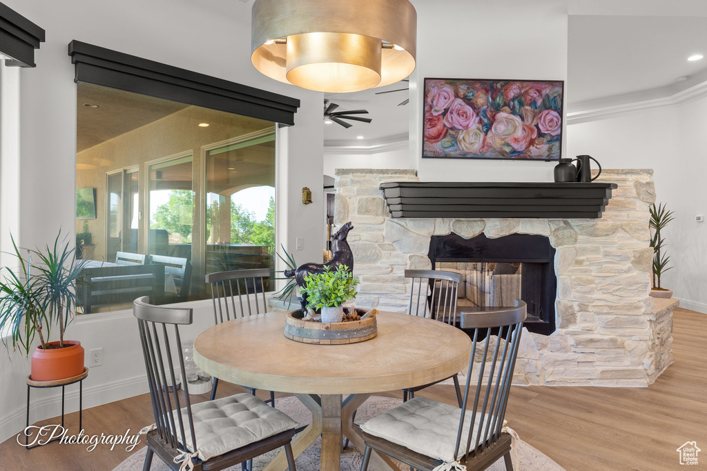 Dining room with ceiling fan, wood finished floors, a stone fireplace, ornamental molding, and baseboards