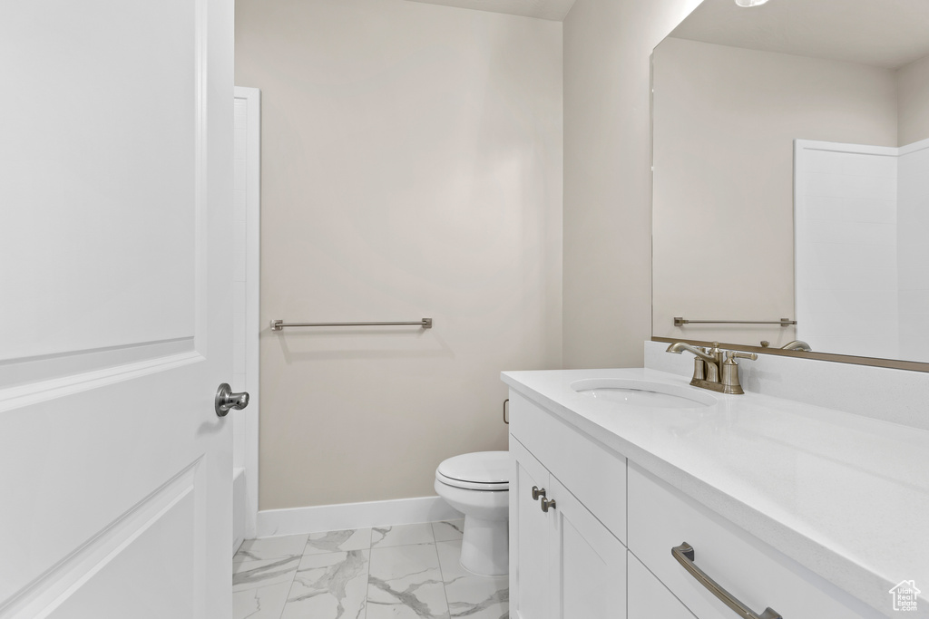 Bathroom featuring marble look tile flooring, vanity, toilet, and baseboards