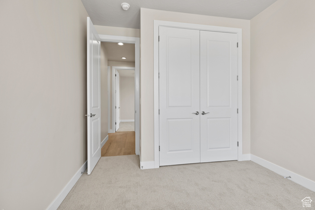 Unfurnished bedroom with light colored carpet, a closet, baseboards, and recessed lighting