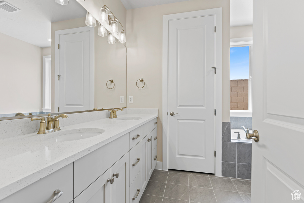 Bathroom with double vanity, tile patterned floors, and tiled bath